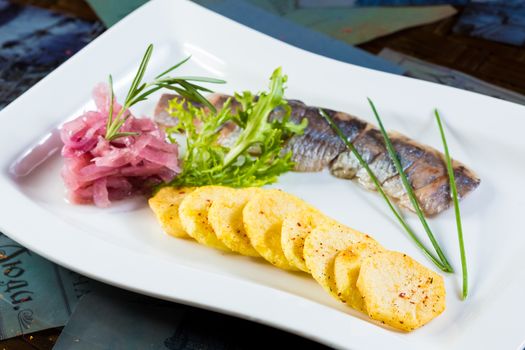 Herring with fried potatoes and red onions on a white plate
