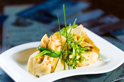 pancakes with meat decorated green onions on a white plate