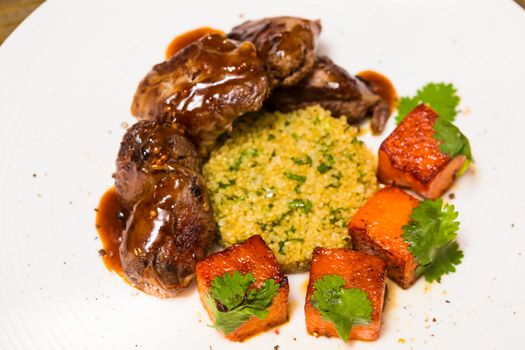 Organic meat of lamb cooked with slices of pumpkin and quinoa in oriental style on a white plate