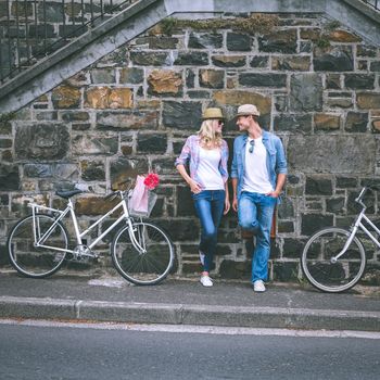 Hip young couple standing by brick wall with their bikes on a sunny day in the city
