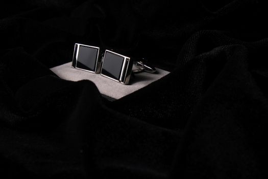 A pair of silver cuff-links showing on black velvet