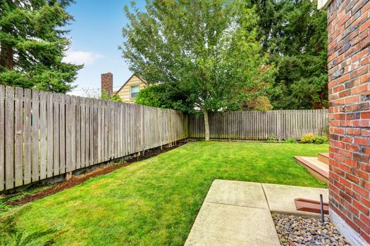 Backyard with wooden fence and walkway. Backyard with green lawn and tree