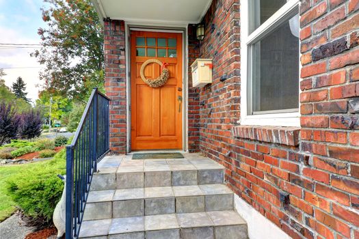 House exterior with brick trim. Entrance porch with orange door and staircase