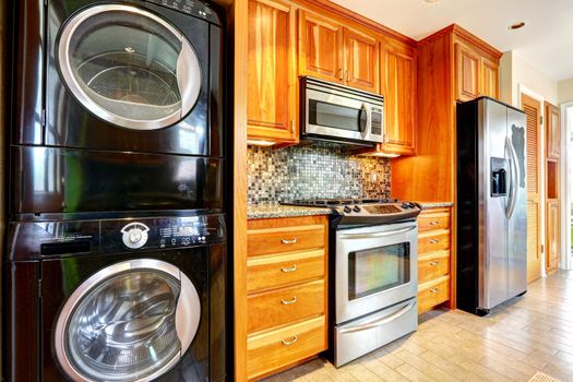 Kitchen maple storage combination with steel kitchen appliances and black laundry appliances