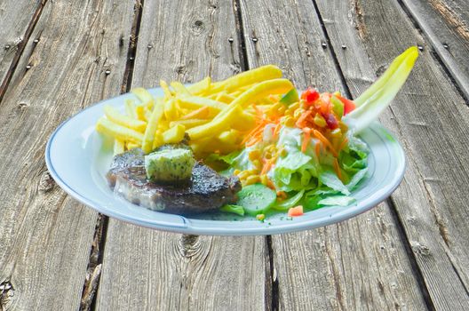 Freshly grilled rum steak with potatoes, french fries garlic butter and salad on a wooden board.