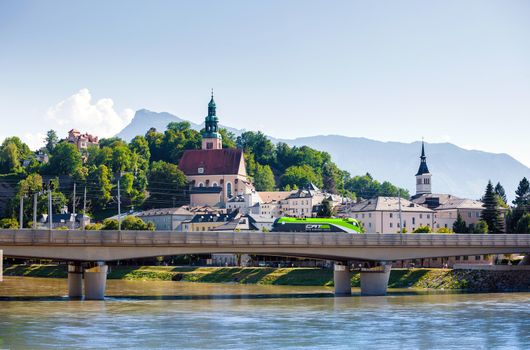 Hallstatt, Austria - August 5, 2013: Electric locomotive crossing the bridge in fron of Pfarramt Mulln catholic church in Salzburg, Austria.