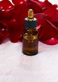 Bottle with oil and red rose petals on a towel. Spa concept