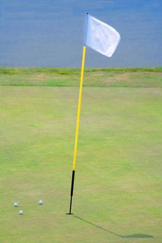 three golf balls on the putting green surrounding hole with a flag