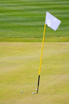 three golf balls on the putting green surrounding hole with a flag