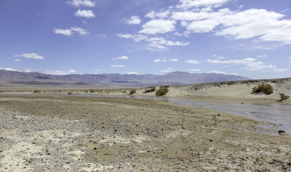 An image of a nearly dried out river bed in the desert with mountains in the distance