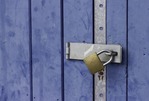 A closed blue slatted door with a secure-looking gold padlock and silver metal re-inforcement bracket fixed to it