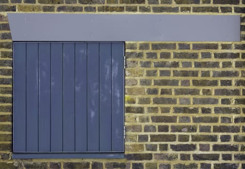 A clean brick wall with a small blue slatted door hatch and pleasing blue/grey beam across the top