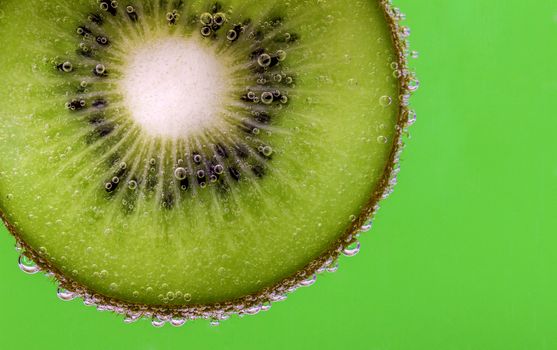 Closeup of a kiwi slice covered in water bubbles against a green background