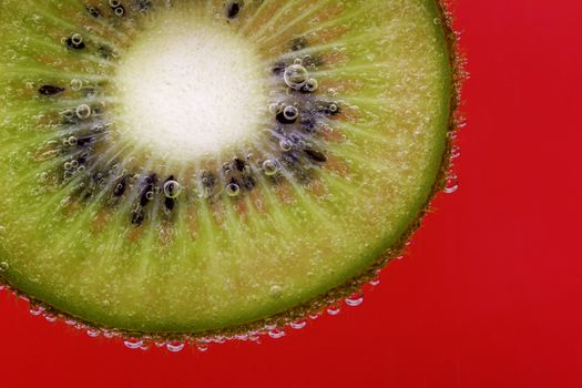 Closeup of a kiwi slice covered in water bubbles against a red background