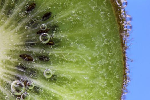 Closeup of a kiwi slice covered in water bubbles against an aqua blue background
