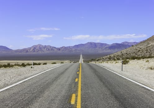 A long open straight road in Death Valley with desert and mountains in the distance