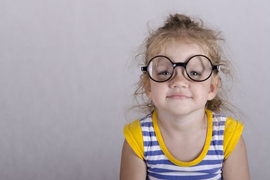 Studio, two-year-old girl sitting on the table, covered with a white cloth, and looking at the picture. Girl dressed funny glasses, hands laid on my knees