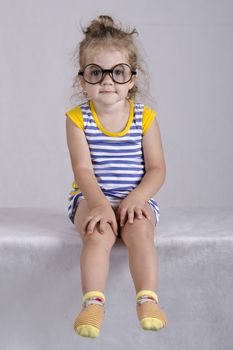 Studio, two-year-old girl sitting on the table, covered with a white cloth, and looking at the picture. Girl dressed funny glasses, hands laid on my knees