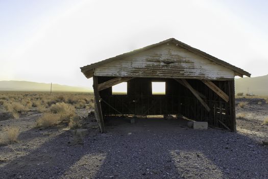 A deserted old rickety hut or shed leaning to one side in the desert with the setting sun creating a silhouette behind