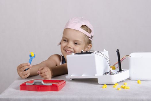 Girl playing in the repairer and repairs toy microwave. A girl Holding a wrench nut and smiles