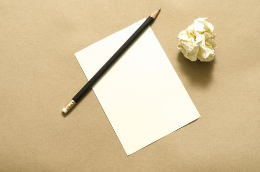 Pencil on clear white paper with crumble paper balls on brown color background