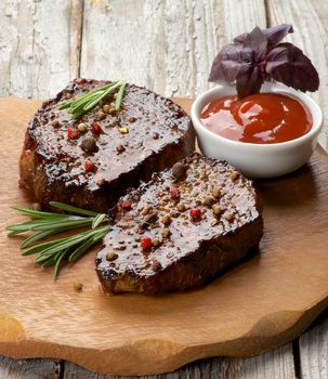 Gourmet Roasted Beef Steaks with Spices, Tomato Sauce and Basil on Wooden Plate on Rustic Wooden background