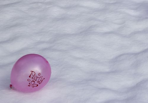 A bright pink/purple balloon with 'Party' written on it lying in the snow