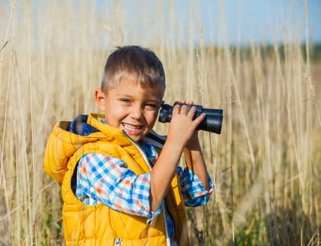 Young boy child playing pretend explorer adventure safari game outdoors with binoculars and bush hat