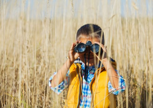 Young boy child playing pretend explorer adventure safari game outdoors with binoculars and bush hat