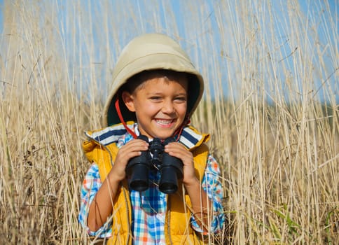 Young boy child playing pretend explorer adventure safari game outdoors with binoculars and bush hat