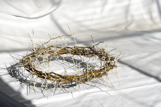 crown of thorns reminds the passion of the christ. resting on a white linen cloth with an olive branch