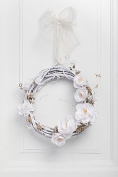 White festive twig wreath of dried vine, painted white and decorated with white paper flowers