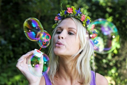 Gorgeous blonde girl with flower garland blowing bubbles outdoors