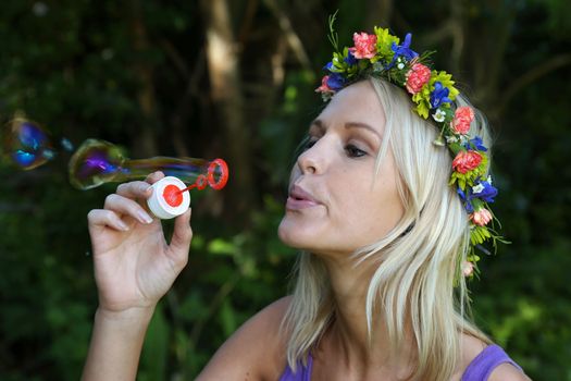 Gorgeous blonde girl with flower garland blowing bubbles outdoors