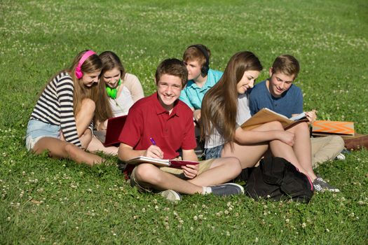 Happy male teenager studying with friends outdoors