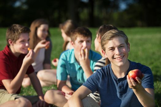 Smiling male teenager with friends holding apple