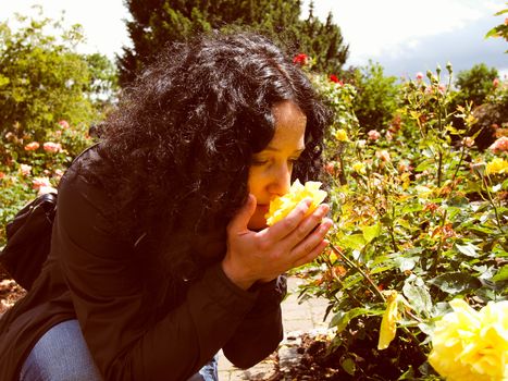 A pretty young brunette girl woman female smelling roses in the garden