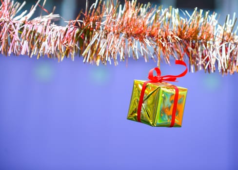 Closeup golden gift box, christmas ornament hanging on tree 