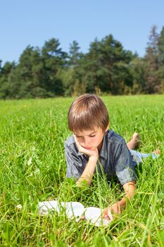 Boy lying in grass reading a book in a summer field