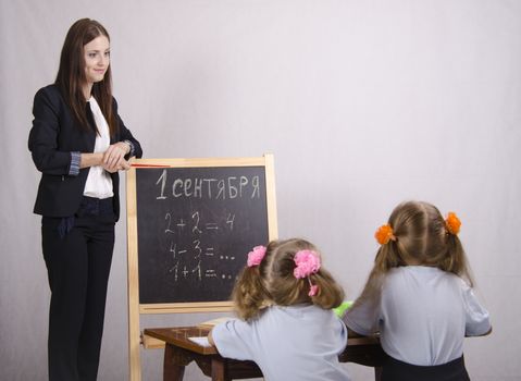 Girl stands at the blackboard, on which is written the 1st of September and a couple of examples and talks about their decision disciples sitting at the table.
