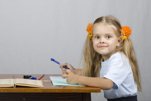 Little girl sitting at the table and writes handle in a notebook. The girl was distracted and looked in the frame