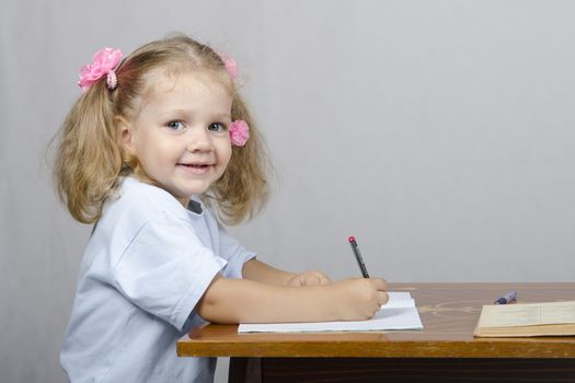 Little girl sitting at the table and writes handle in a notebook. The girl was distracted and looked to the right.