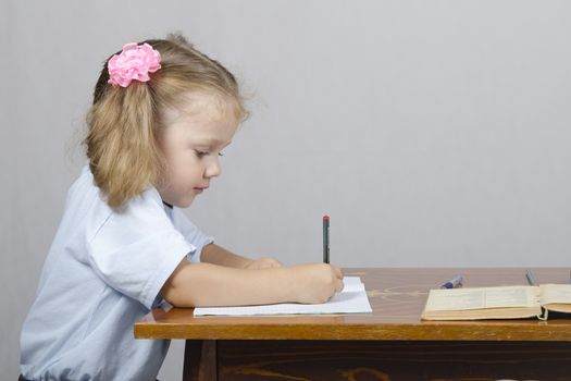 Little girl sitting at the table and writes handle in a notebook. The girl was distracted and looked to the right.