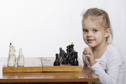The girl sitting at the table, on which stands the chess Board. The girl is learning how to play chess