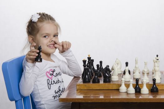 Four-year-old girl playing in chess. A girl holding a hand shape, finger of the other hand tucked into the nose. Fun looking in the frame