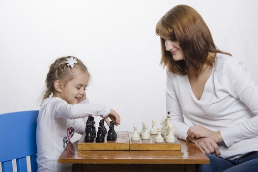 Mom and daughter playing at a table in chess. Mother teaches daughter game