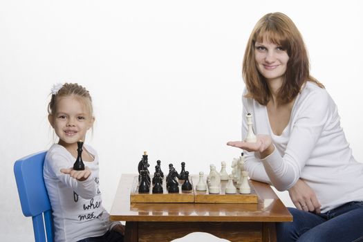 Mother and four-year-old daughter sitting at a table and play chess. Mom tells about the shapes