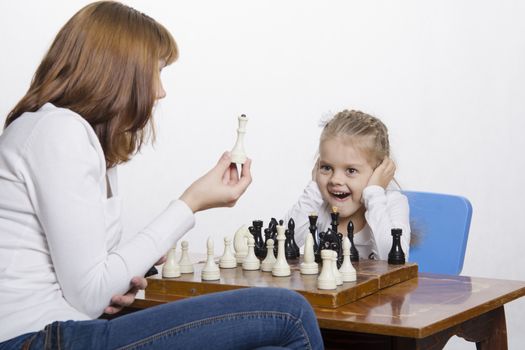 Mother and four-year-old daughter sitting at a table and play chess. Mom tells about the shapes