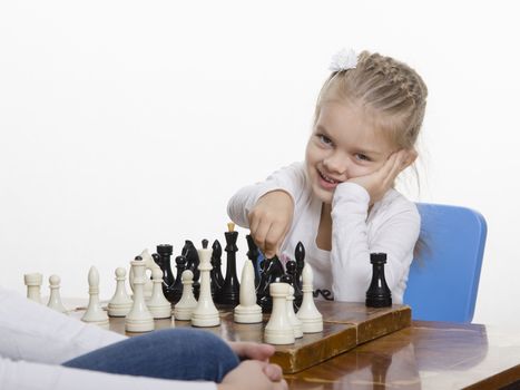 Four-year-old girl playing in chess. Girl fun looking into the frame with the figure in hand, preparing to make a move