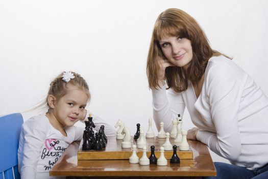 Mom and daughter playing at a table in chess. Mother teaches daughter game